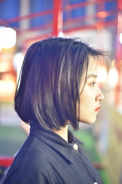 A woman with a short bob hairstyle, inspired by a Korean drama character. Her bob is slightly layered and styled with a gentle curve, framing her face. She has soft, side-swept bangs that add to the overall chic and youthful look.