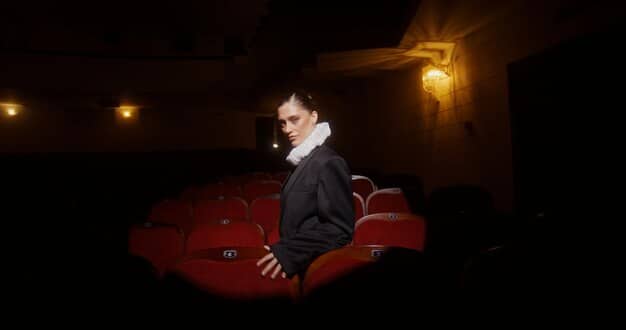 A critic sitting in a darkened theater, illuminated only by the faint glow of their laptop screen as they take notes during a performance, capturing the dedication and immediacy required in live drama reviewing.