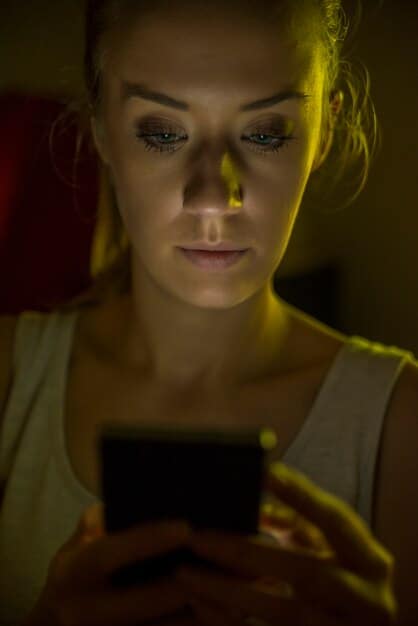 A close-up shot of a person's face illuminated by the glow of a smartphone screen. The person's expression is a mix of anxiety and fascination. The image is intended to evoke a sense of the pervasive influence of technology on our lives and the potential for both connection and isolation.
