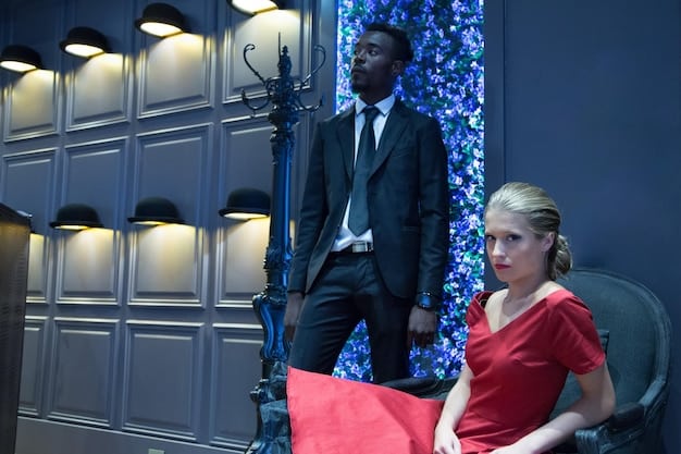 A candid shot of two actors on set, one looking enviously at the other, who is receiving positive attention from the director. The scene conveys subtle competition and underlying tension.